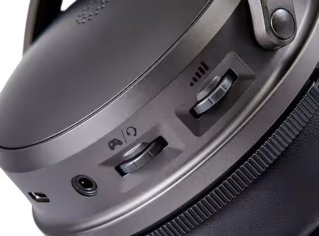 Primo piano del fianco del padiglione di una cuffia grigio antracite, con due levette scorrevoli contrassegnate dalle icone del bilanciamento gioco e chat e del volume, un connettore jack da 3,5 mm e una porta USB-C.